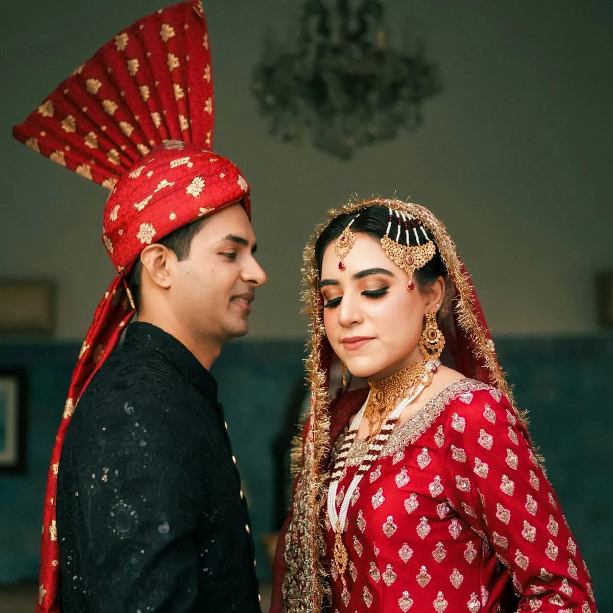 Armaan looking at Devika, her eyes lowered, in a quiet room with a chandelier